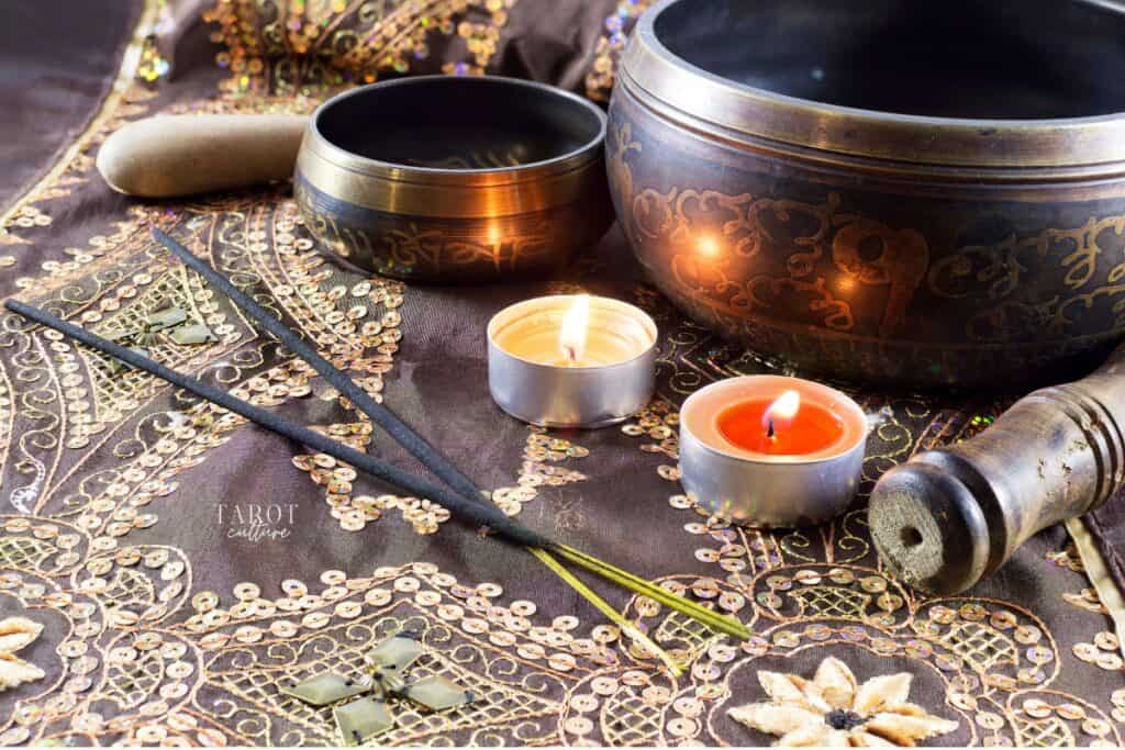 Two singing bowls, one big and one small, over a piece of purple fabric, with two burning candles and two incense sticks