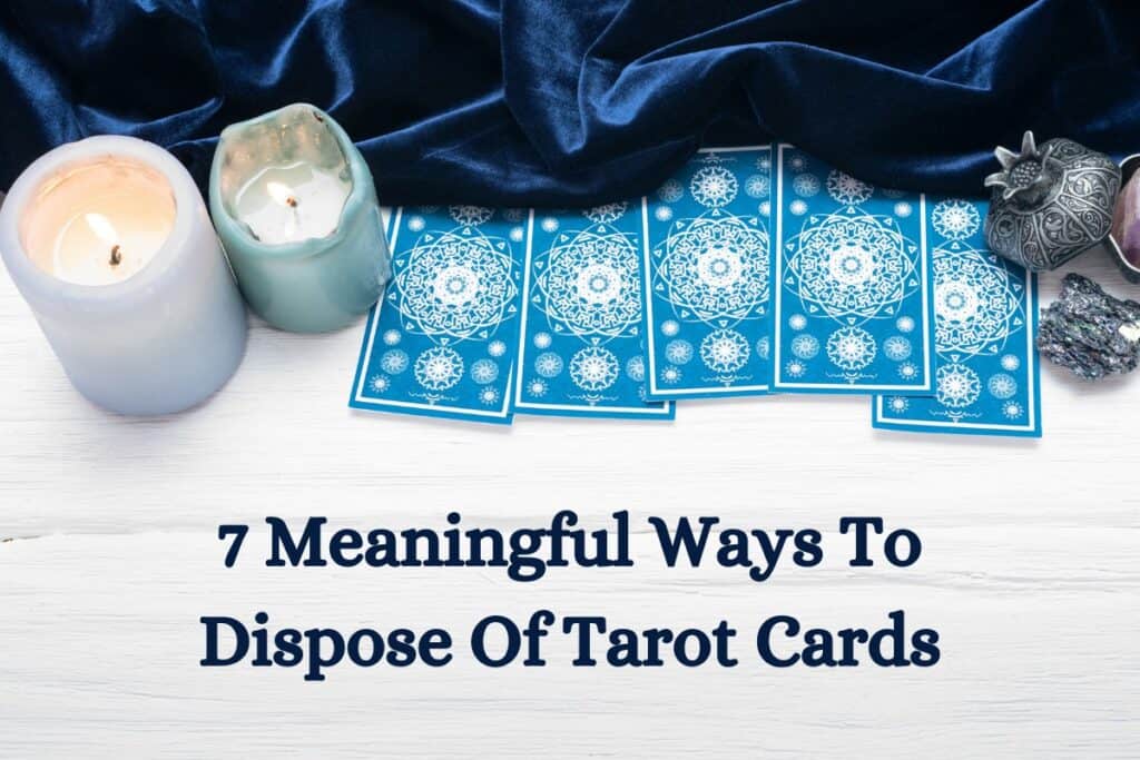 A piece of blue velvet, two burning candles, a pyrite and blue Tarot cards over white wooden table with caption "7 meaningful ways to dispose of tarot cards"
