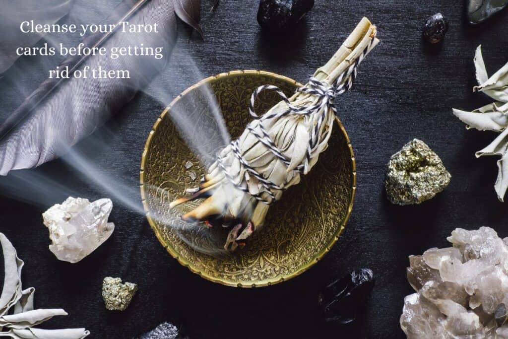 Gemstones, crystals a feather, sage leaves and a burning smudge stick in a golden pot, with the caption: "Cleanse your Tarot cards before getting rid of them"